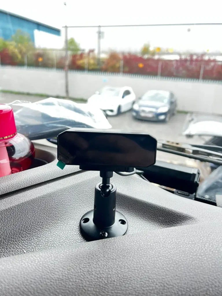 Compact tracking device mounted on a vehicle dashboard with a windscreen view of a car park