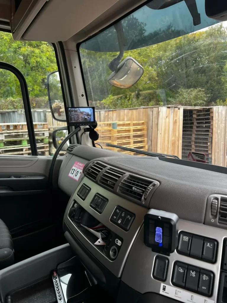 Small in-cab camera monitor mounted near the mirror above an HGV dashboard, with a vehicle height warning sticker